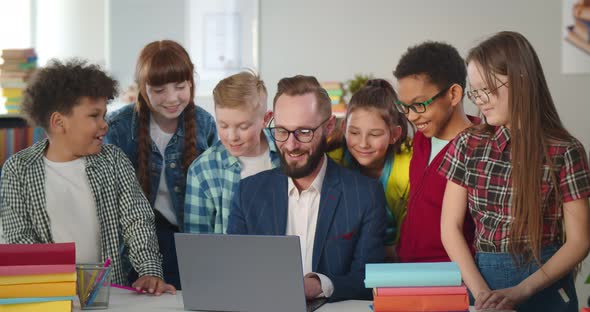 Male Teacher in Glasses Showing Scientific Video to Joyful Children Using Laptop