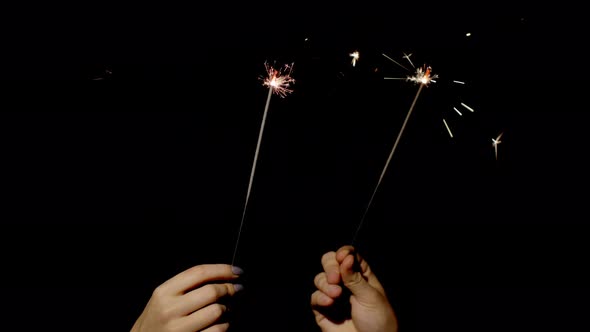 Close-up of Hands Holding and Waving Bengal Fire Burning Sparklers in Front of Black Background