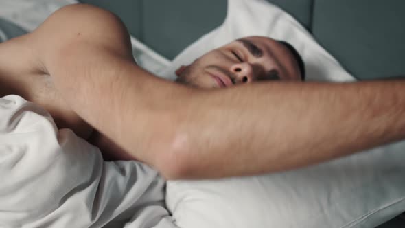 Close Up Shot of Sleepy Caucasian Man Waking Up in the Morning, Taking a Smartphone From the Bedside