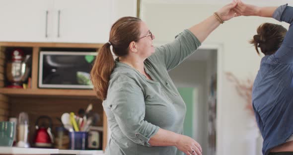 Caucasian lesbian couple smiling and dancing in kitchen