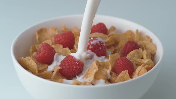Corn flakes with raspberry in a bowl pouring with milk. Slow Motion.