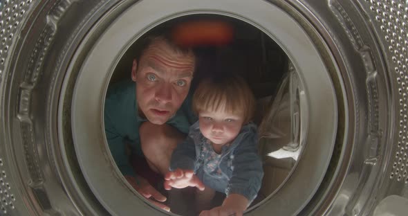 Small Child Looks Into Inside of Washing Machine with Dad