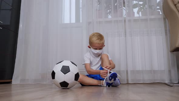 A Little Boy Sits on the Floor and Learns to Tie the Laces on Football Boots