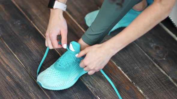 Closeup Female Hands Lacing Shoelaces on Sneakers Standing on Wooden Floor High Angle