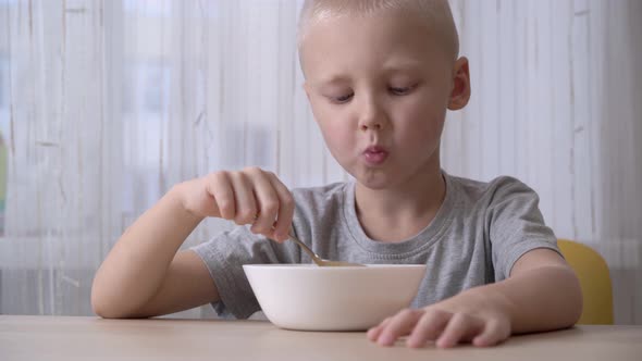 Cute satisfied little boy eating cereal with milk for breakfast.