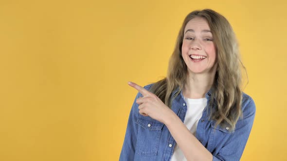 Portrait of Pretty Girl Pointing with Finger on Side Yellow Background
