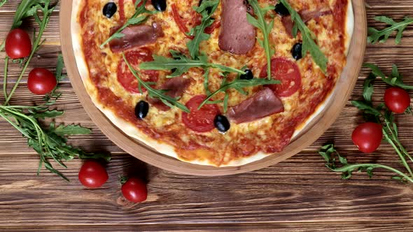 Italian pizza with ham, tomatoes, olives and basil on wooden table. Top view