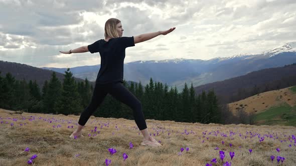 Young Woman Doing Yoga Virabhadrasana  Warrior Pose on Valley of High Mountain Among Crocus Flowers