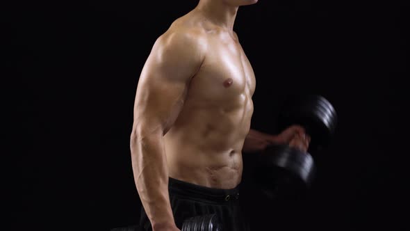 Man Flexes His Hands with Dumbbells Training His Biceps on a Black Background in the Studio