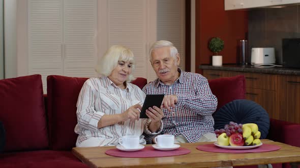 Senior Old Couple Grandparents Talking and Using Digital Tablet Computer at Home. Internet Shopping