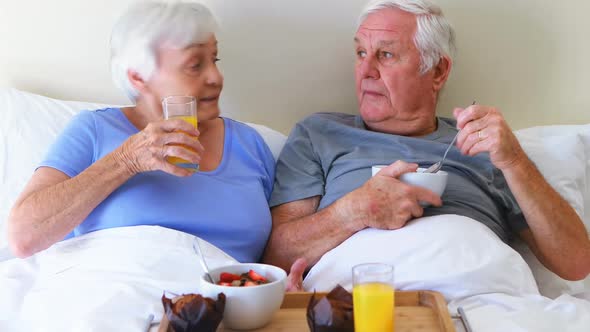 Smiling couple having breakfast on bed