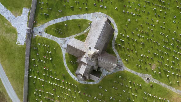 Top View Of Snow-Covered Roof Of Lom Stave Church With Cemetery In Lawn At Norway. Aerial Orbiting