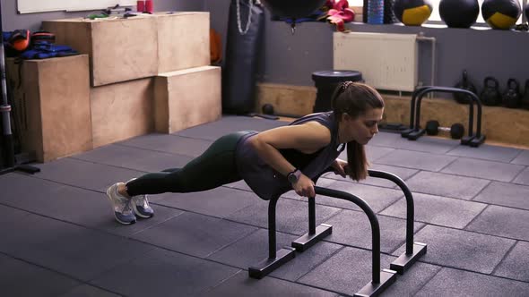 Attractive Sportive Brunette Girl Doing Push Ups Using Pushup Bars at the Gym