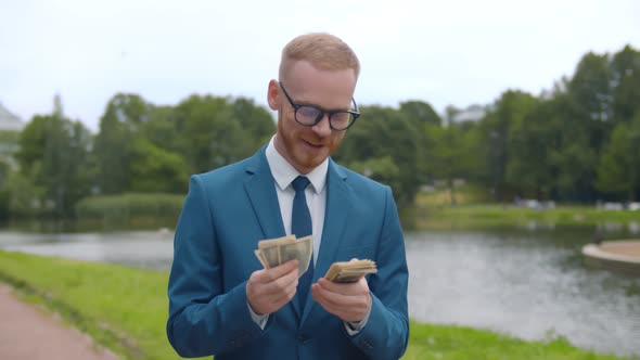 Young Businessman Holding Money in Hand Counting Income Strolling in Summer Park