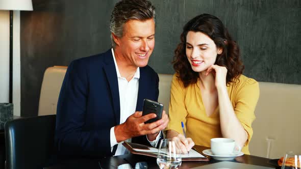 Smiling businessman and colleague discussing over mobile phone