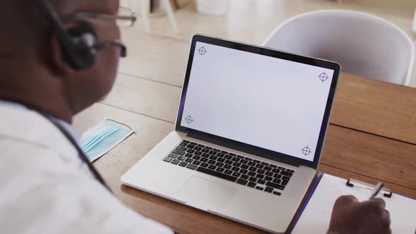 African american male doctor making video consultation wearing headset using laptop with copy space