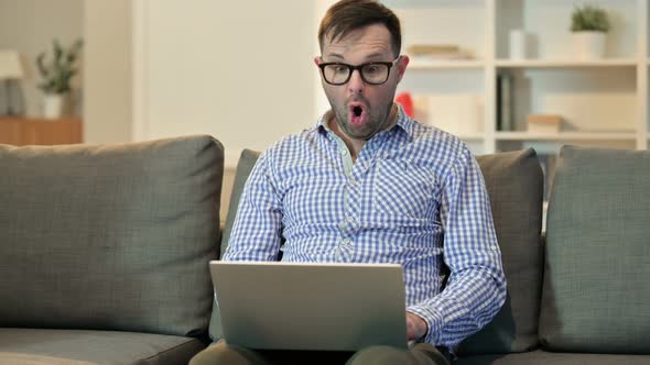 Young Man with Laptop Feeling Shocked at Home 