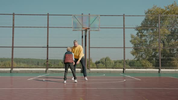 Boy Throwing Ball Playing with Father on the Basketball Court on a Sunny Day