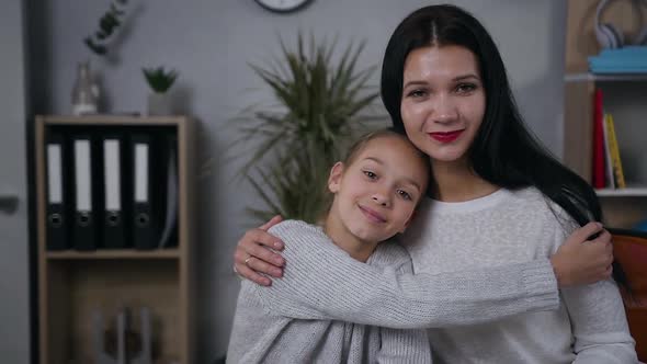 Mother and Teen Daughter Hugging Each other and Looking at Camera at Home