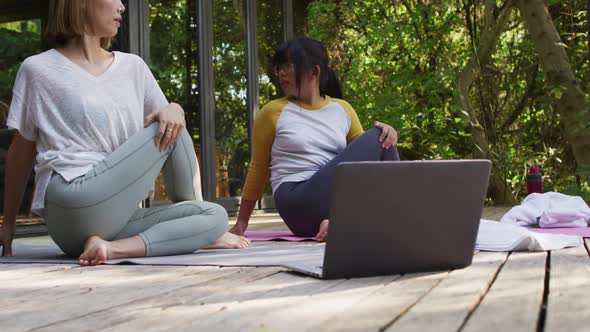 Asian mother and daughter practicing yoga outdoors in garden with laptop