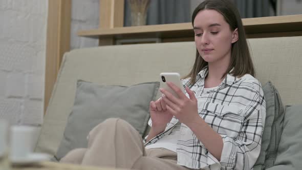 Beautiful Young Woman Sitting on Sofa and Using Smartphone 