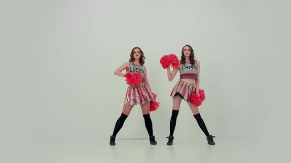 Two Uniformed Cheerleaders with Red Pompoms Dance an Uplifting Dance Move Their Hips