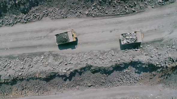 Mining Dump Trucks in Large Granite Open Pit Mine. Loaded Trucks Rides on Road Quarry Ledge Drone