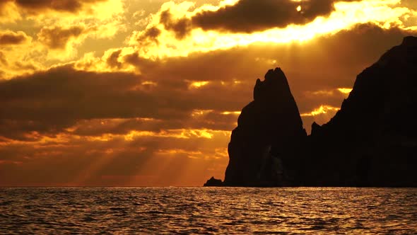 A Red Burning Sunset with the Silhouette of a Cliff Over the Sea