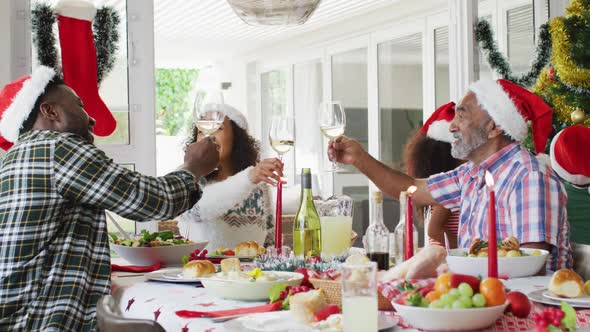 Happy african american multi generation family wearing santa hats and celebrating holiday meal