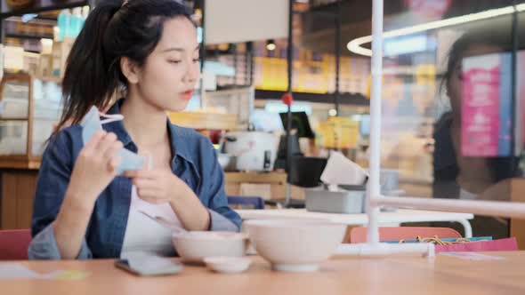 Asian woman sitting separated in restaurant eating food .