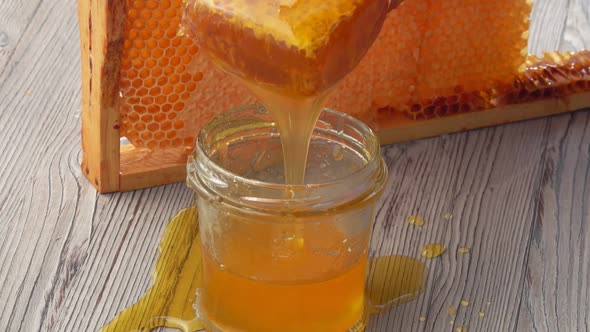 Honey is Flowing Into the Glass Jar on the Background of a Frame with Honeycombs