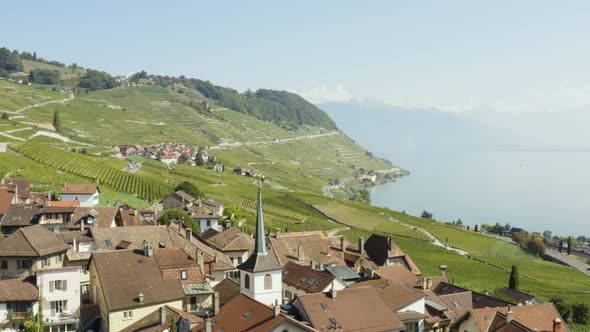 Overflying typical swiss village (Riex) in Lavaux vineyard, passing close to church bell tower - Swi