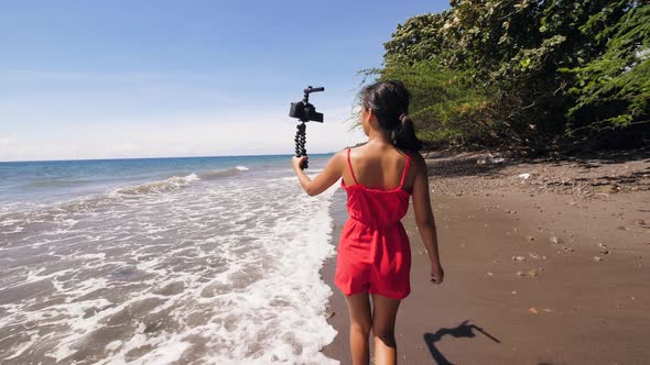 Back View of a Female Vlogger Walking and Recording a Selfie Video on the Beach