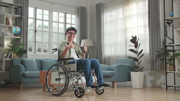 Asian Man Sitting In A Wheelchair Smiling And Showing Thumbs Up In Living Room