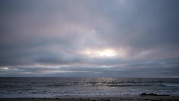 Seabirds run along the shore as sun sets over the ocean on a gloomy day - time lapse