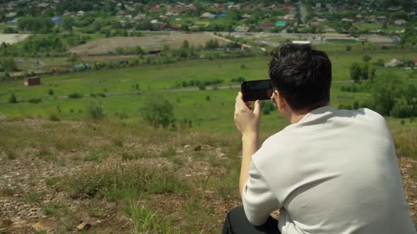 A Young Adult Male Takes a Smartphone Picture From the Top of a Large Hill