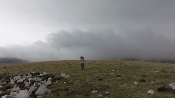 A Slender Young Woman in Travel Clothes Walks and Runs on a High Plateau in Foggy Weather Against