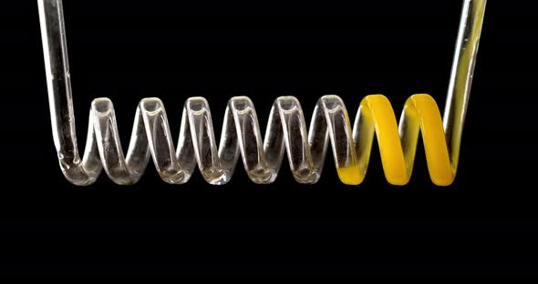 The Yellow Liquid Fills the Spiral of Glass on a Black Background in Slow Motion. Chemical Capacitor