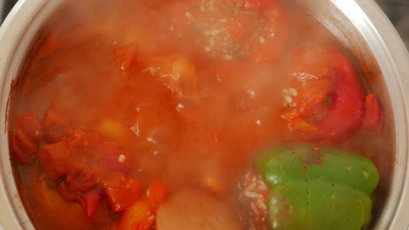 Cook Stirring Pan with Boiling Red Peppers Stuffed with Rice and Minced Meat - Top Down View