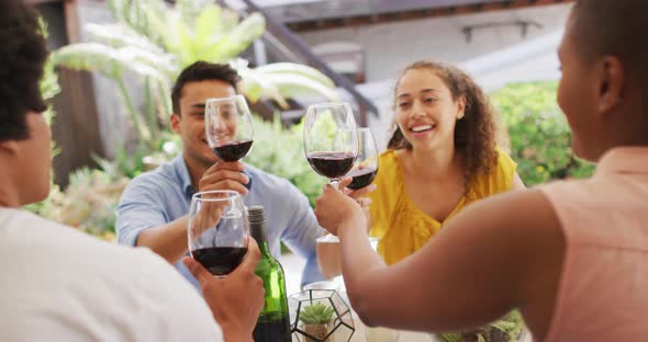 Group of diverse male and female friends laughing and toasting with wine at dinner party on patio