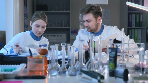 Male Medical Scientist in Lab Coat Talking to Female Colleague Making Notes Laughing Friendly Spbas