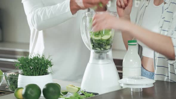 Vegetarianism Young Couple Prepares a Smoothies in the Kitchen Man and Woman Puts the Green