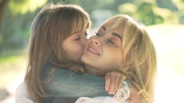 Closeup Portrait of Smiling Caucasian Woman Looking at Camera As Girl Kissing Cheek in Slow Motion