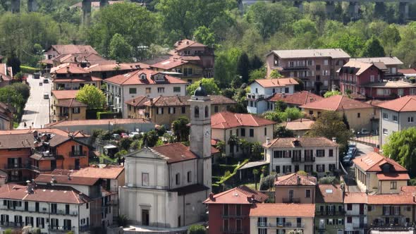 Close up of a small village church in an Italian village with old red tiled roofs and lush green tre