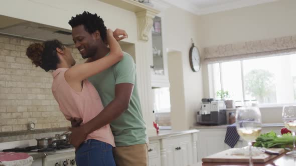 Happy biracial couple hugging in kitchen while cooking