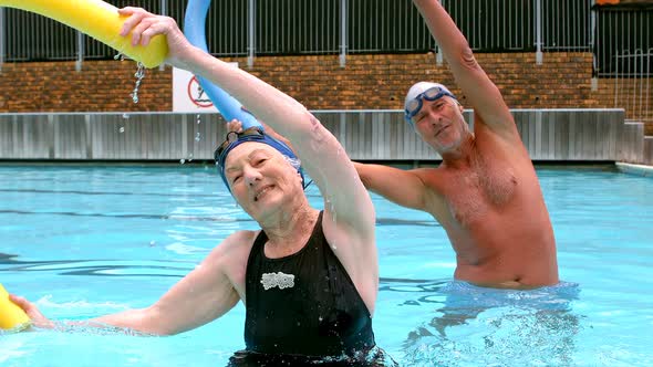 Senior couple exercising with pool noodle in swimming pool