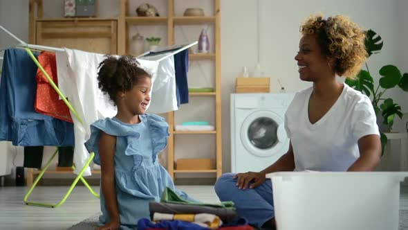 Young American Woman and Little Girl Having Fun and Sitting on Floor in Laundry Room at Home Spbd