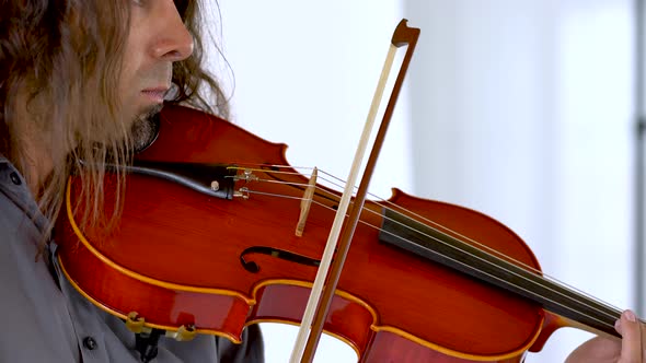 Close up profile of hispanic male musician with long hair and goatee playing red viola