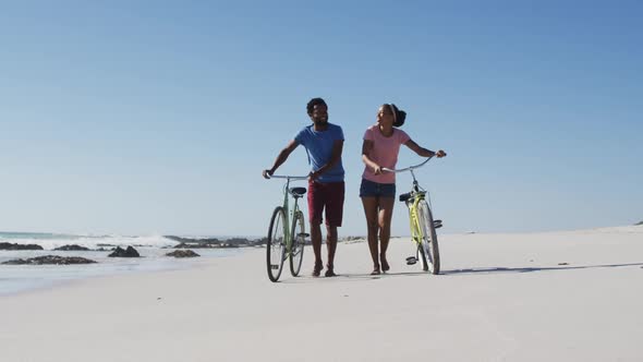 African american couple walking with bikes on the beach