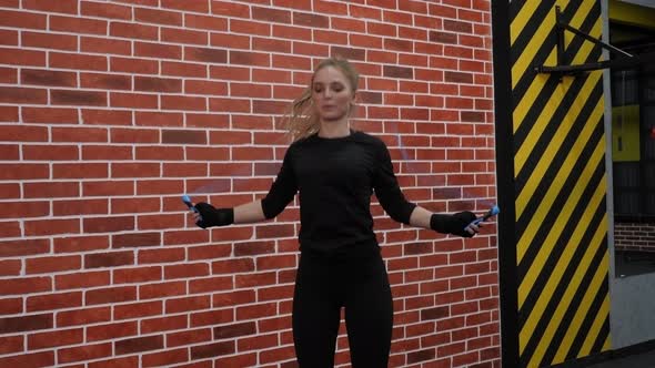 An Active Girl Jumps on a Rope in the Gym Against the Background of a Brick Wall